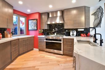 A modern kitchen with warm wood cabinetry, red accent walls, stainless steel appliances, and white marble countertops at Park City Main Street Retreat.
