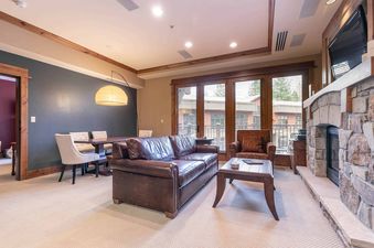 A living room with a fireplace and a leather sofa and armchairs, with access to a patio through sliding glass doors.