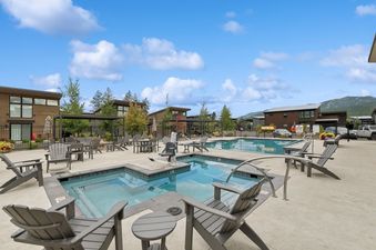 A sunny day view of the community pool and hot tub area at Quarry A25, surrounded by comfortable lounge chairs and modern buildings, with mountains in the background.