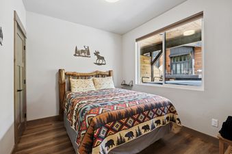 A cozy bedroom at Pioneer Peak featuring a bed with a rustic wooden frame and a vibrant, patterned quilt, complemented by wildlife-themed wall art and a large window overlooking the outdoor area.