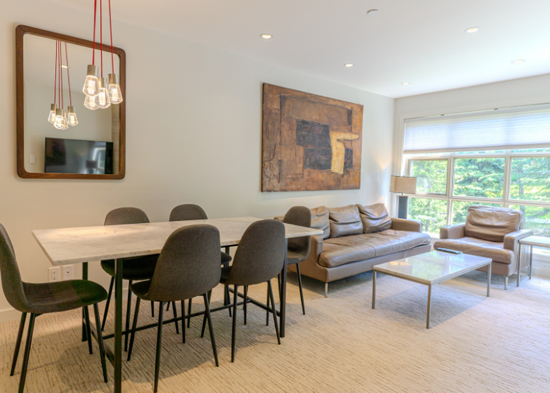 The dining and living area features a modern dining table, comfortable seating, and a large window offering an exterior view.