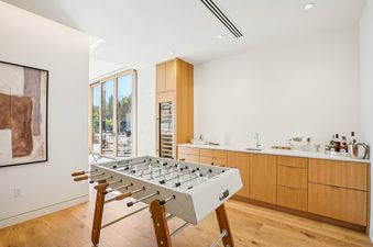 A modern game room with a foosball table, wet bar, and large glass doors leading to an outdoor area.