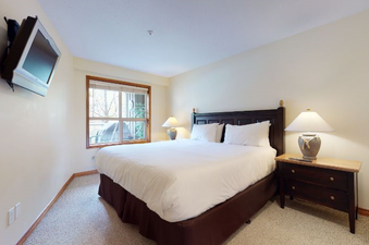 The primary bedroom features a comfortable queen-size bed with crisp white linens and a dark wooden headboard.