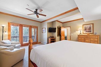 A spacious bedroom featuring a large bed, two armchairs, a wooden dresser, and balcony access through decorative glass doors.