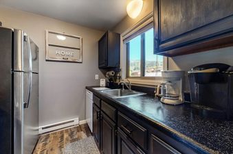 A kitchen with a stainless steel refrigerator, a coffee maker, a toaster, and a sink. The window in the background overlooks a wooded area.