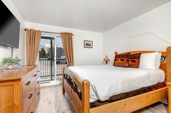 The bedroom of Suncreek A7 with a wooden bed, white bedding, and a balcony overlooking snow-capped mountains.