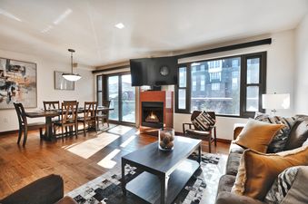 A spacious and elegantly furnished living and dining area at the Lowell 303, featuring a dining table, a comfortable sofa, a fireplace, and large windows with an outdoor view.