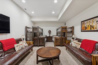 A cozy bunk room in Slopeside 111 with two wooden bunk beds, two brown leather sofas, and a round wooden coffee table, illuminated by soft lighting.