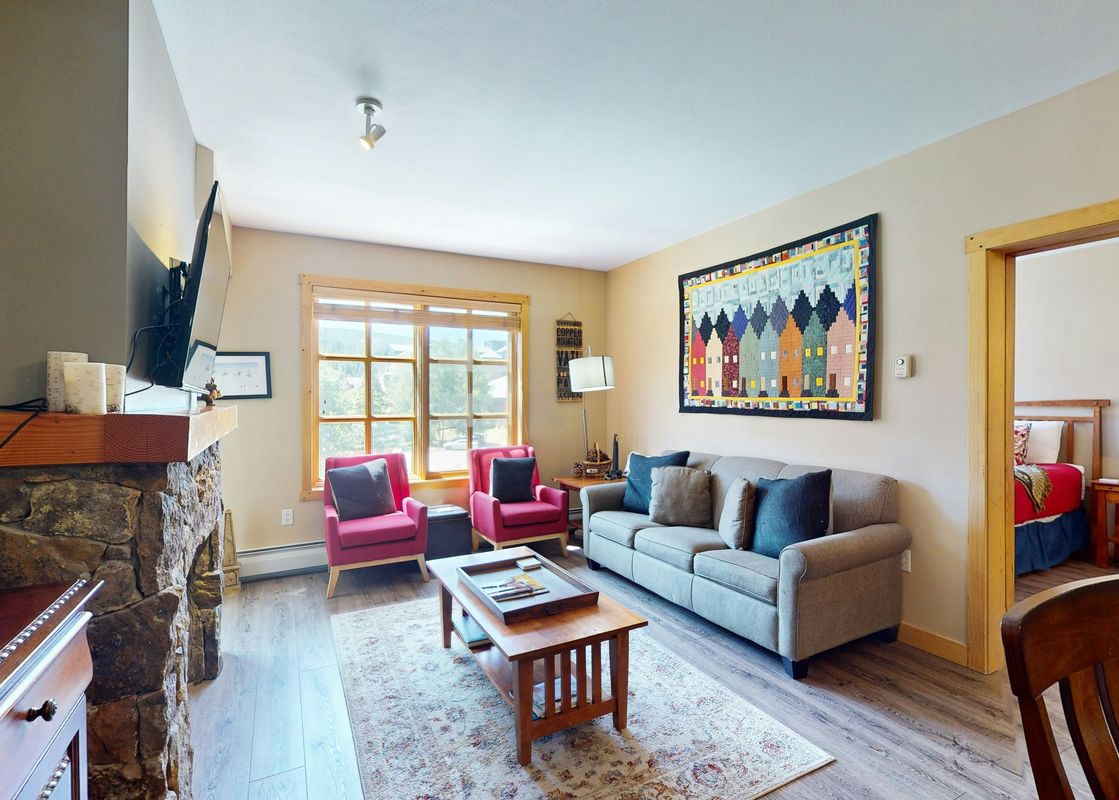 A living room with a couch, two armchairs, a coffee table, a fireplace, a television and a doorway leading to another room.