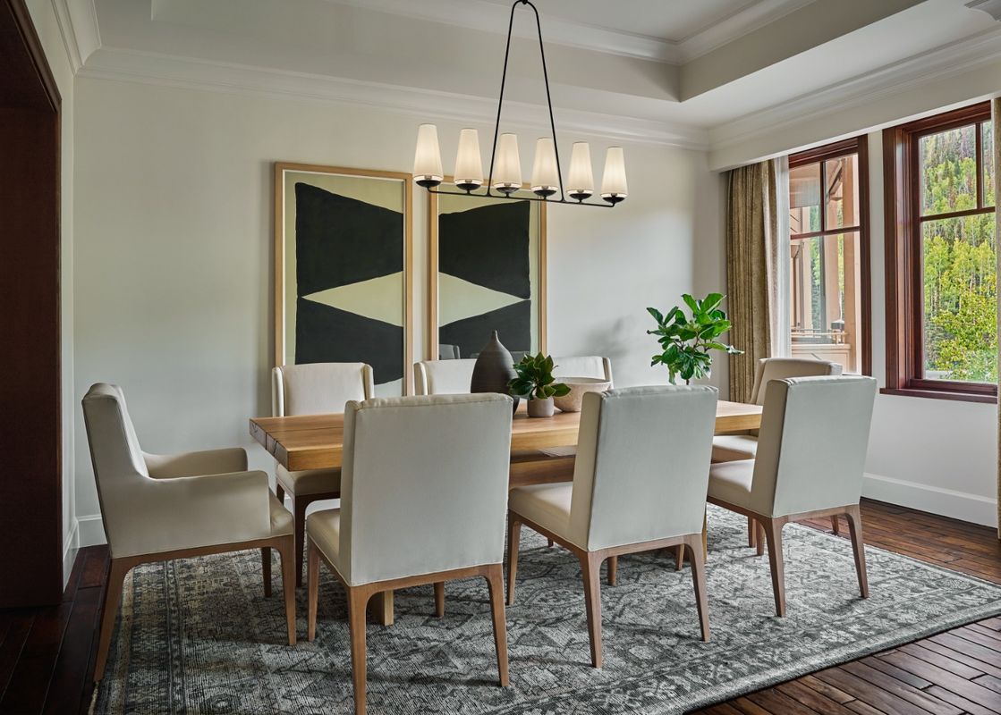 An elegant dining room in the Montage Three Bedroom Residence Resort View features a large wooden dining table surrounded by cream-colored upholstered chairs, with two large abstract paintings on the wall and a modern chandelier overhead.