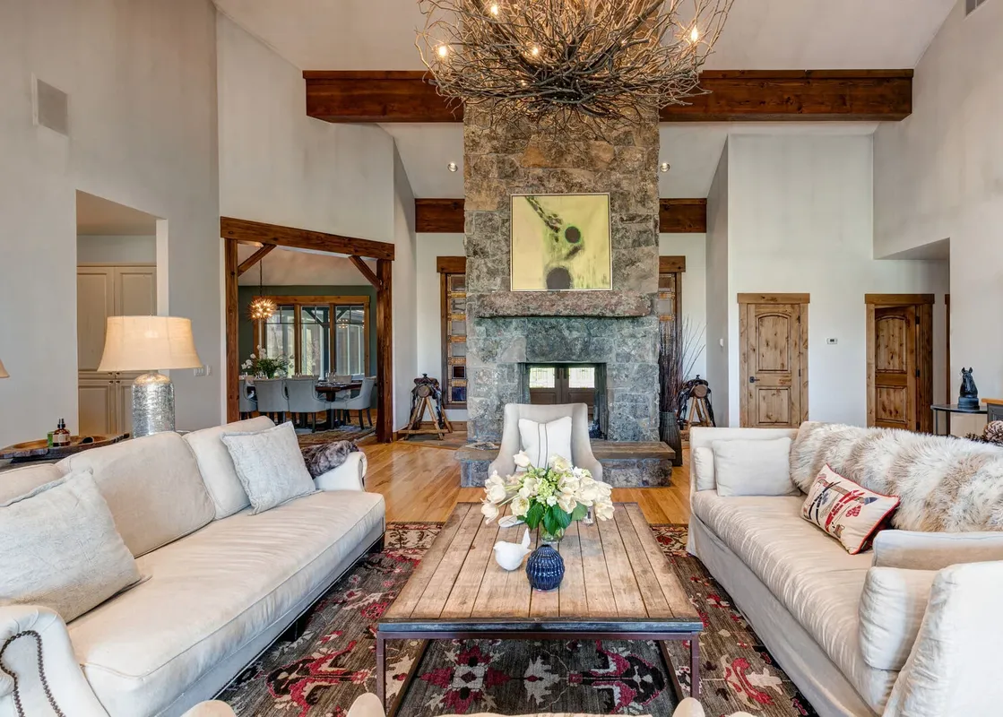 A living room with a large stone fireplace, two white sofas, and a coffee table with flowers in a vase.