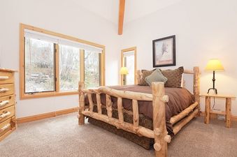 The bedroom in Timberlake 341 features a rustic log bed, a dresser, and a large window looking out onto a wooded area.