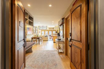 A wide-angle view from the main entrance of Royal Plaza 403, showcasing a large hallway with wooden floors and an oriental rug, leading into an open-plan living and dining area decorated with American flag art and a Salt Lake 2002 poster.