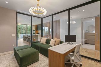 The home office at Founders Place 1504, featuring a green velvet sofa, a white marble-topped desk, and glass doors opening to a scenic outdoor view.