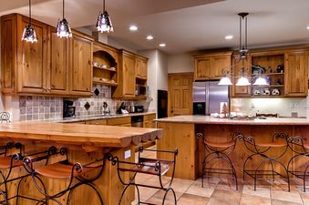 A rustic kitchen is shown with natural wood cabinets, granite countertops, and multiple pendant lights illuminating the space.