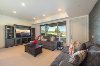 A comfortable living area in Juniper 801 with a large flat-screen TV, dark wood furniture, and expansive windows showcasing a scenic outdoor view.