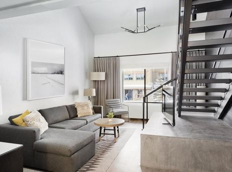 Modern living area in the Gravity Haus JH Loft with a gray sectional sofa, concrete details, and an open staircase.
