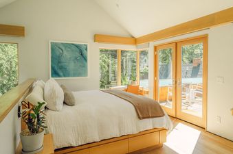The bedroom at Silver Queen Chalet features a large bed with plush bedding, a large window with views of the surrounding forest, and a cozy armchair perfect for relaxing.