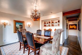 An elegant dining room featuring a dark wood table with black leather and patterned fabric chairs, illuminated by a grand chandelier, with a large painting and decorative display shelving.