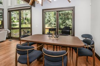 A modern dining room in Chateau Tremonte 8 featuring a dark wood table with six chairs, a sculptural centerpiece, and large windows offering views of a lush outdoor landscape.