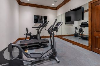 A private home gym at Ridgepoint Retreat features an elliptical machine, a recumbent bike, and a treadmill, with wall-mounted TVs and a large mirror.