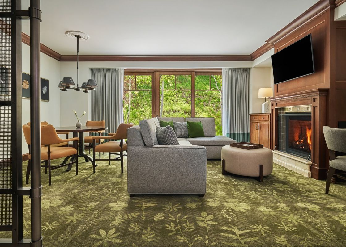 A spacious and inviting living area in the Montage Deer Valley Accessible Resort View King Suite with Fire Pit, featuring comfortable seating, a dining area, and a large window overlooking lush greenery.