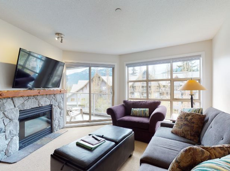 A cozy living room in Aspens on Blackcomb Unit 461 with a stone fireplace, television, and comfortable seating.