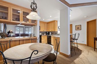 A cozy kitchen and dining area in The Charter F2105 with light wood cabinetry, a round dining table, and a breakfast bar with stools.