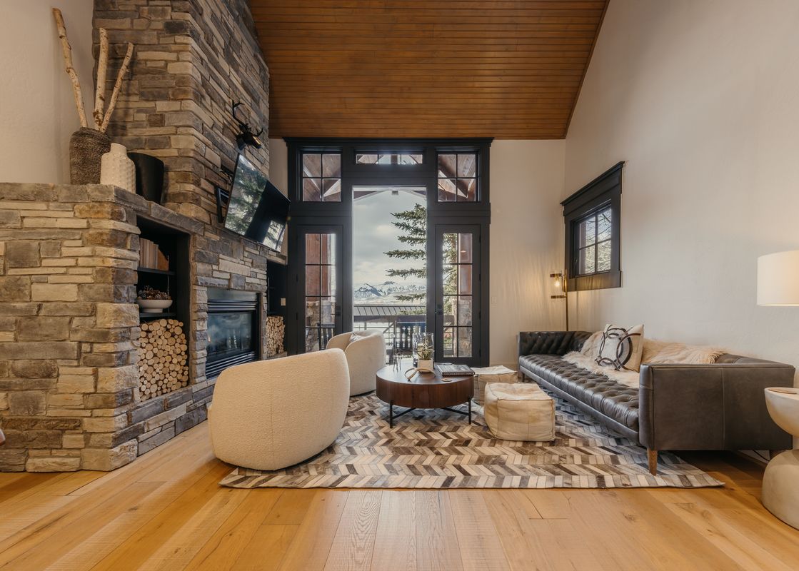 Cozy living room at Campfire Cabin at See Forever featuring a massive stone fireplace, elegant seating, and floor-to-ceiling windows showing mountain views.