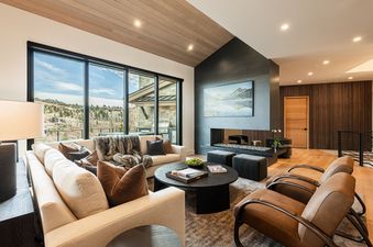 A modern and luxurious living room at Deer Valley Luxe at Moonshadow featuring a fireplace, plush seating, and scenic mountain views through large windows.