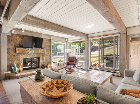 A spacious and bright living room at Enclave 207 with a stone fireplace, large TV, comfortable sofas, and outdoor views.
