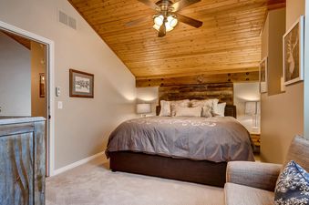 A cozy bedroom with a king-sized bed, wooden ceiling, and a ceiling fan, featuring rustic and modern decor.