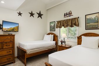 A cozy twin bedroom at Vantage Point 504 with two wooden-framed beds, a wall-mounted TV, wooden dresser, and framed artwork.