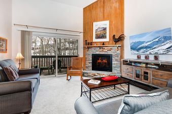 The spacious living room at Snow Flower 152 Park City, featuring a large flat-screen TV, fireplace, and sliding glass doors leading to a balcony with winter views.