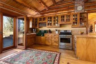 A rustic cabin kitchen at 7 Cabins Jackson Hole with wooden cabinets, a stainless steel stove, and a door opening to a patio.