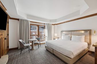 The spacious and inviting bedroom at The Aspen 44A, featuring a large bed, a small seating area, and windows with a view of the snowy outdoors.