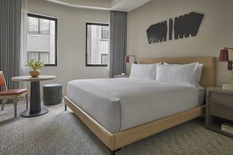 Pendry Two Bedroom Resort King Residences, showing a king-sized bed with a white duvet cover and a tan headboard, as well as a nightstand and a bedside lamp.