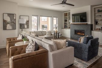 The living area of Beaverhead Condo 301 features a cozy fireplace, ample seating with light-colored sectionals and dark leather armchairs, and large windows offering exterior views.
