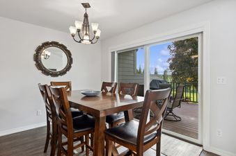 The dining area at Tee Time features a dark wood table with six chairs, a round mirror on the wall, and a sliding glass door leading to an outdoor deck.