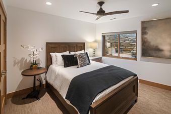 A cozy bedroom at Silver Lode Escape features a large wooden bed with white linens, dark pillows, and a ceiling fan, illuminated by recessed lighting.