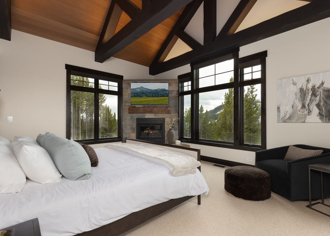 The master bedroom at Summit View Chalet Big Sky features a king bed, fireplace, television, and stunning mountain views from large windows.