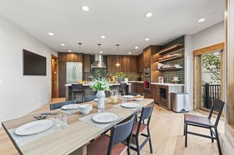 The dining area and kitchen of Pinnacle in Deer Valley are illuminated by recessed ceiling lights, showcasing a modern open-concept design with light wood floors and dark wood cabinetry.