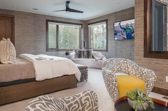A luxurious bedroom at Over the Edge with a large bed, two armchairs, a curved sofa, and large windows offering a view of snowy trees.