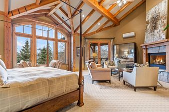 A luxurious master bedroom at Oak Wood Lodge with a four-poster bed, a fireplace, and large windows overlooking a scenic mountain view.