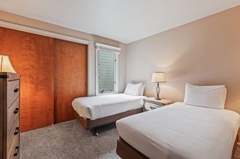 A cozy twin bedroom at Snow Flower 107 Park City with two beds, a nightstand, and a wooden closet.