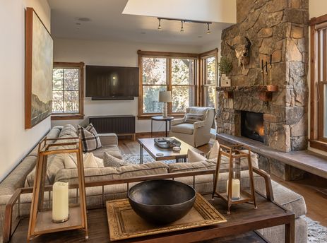 A cozy living room at Essentia Townhome 151B with a stone fireplace, comfortable seating, and large windows offering views of the outdoors.