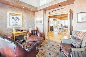 A cozy, rustic living area at Trails Edge Vacation Home with leather and fabric armchairs, art on textured walls, and a view into an adjacent room.