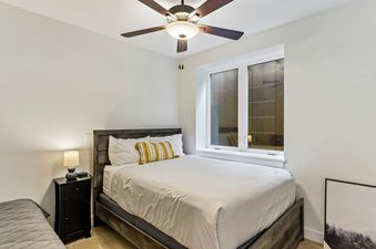 A bedroom with a bed, a side table with a lamp, and a window with an exterior view.