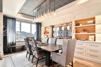 A modern dining room with a long wooden table, ten clear glass pendant lights hanging above it, and built-in white cabinets with open shelves displaying decorative items.
