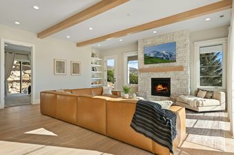 A spacious and inviting living room in the TimpView Bundle, featuring a large tan leather sectional, a stone fireplace with a TV mounted above, and light wood flooring.